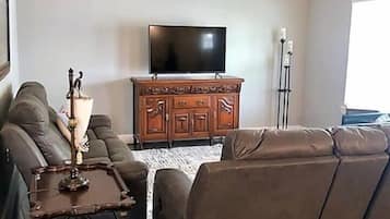 A living room with a brown leather sofa, a wooden cabinet, a flat-screen TV, and a ceiling fan.