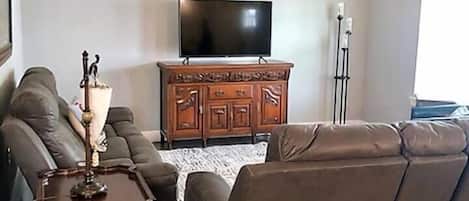 Una sala de estar con un sofá de cuero marrón, un armario de madera, un televisor de pantalla plana y un ventilador de techo.