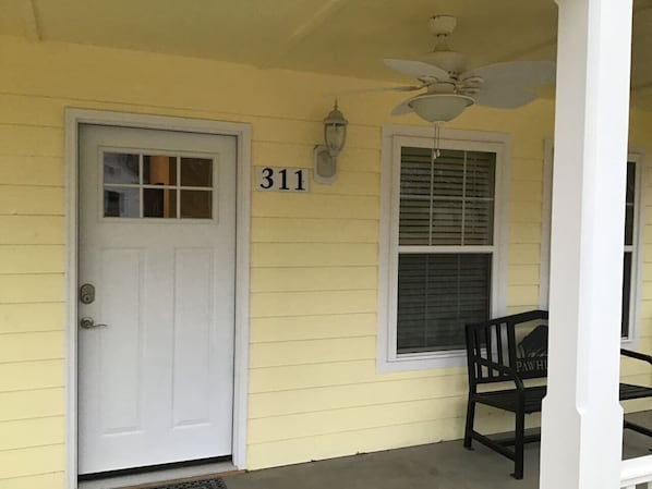 A yellow house with a white door, a window with shutters, and a number '311' on the wall.