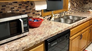 A kitchen with wooden cabinets, a microwave, a dishwasher, and a tiled backsplash. - MJ’S BUNKHOUSE #3-2 BLOCKS TO DOWNTOWN (Pawhuska)