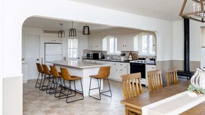 A modern kitchen with white cabinetry, a central island, bar stools, and a dining table with chairs. - Spacious & Quiet Amish Farm Stay - 16+ Guests (Leola)