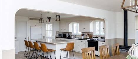 A modern kitchen with white cabinetry, a central island, bar stools, and a dining table with chairs.