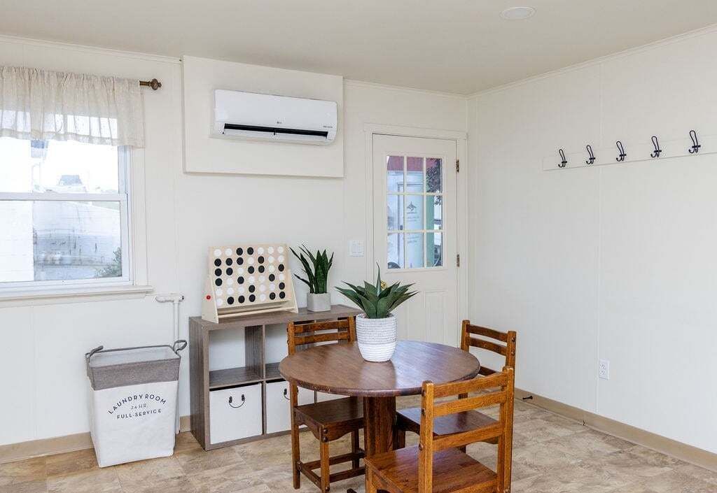 A room with a wooden dining table, chairs, a potted plant, a laundry basket, and a wall-mounted air conditioner.