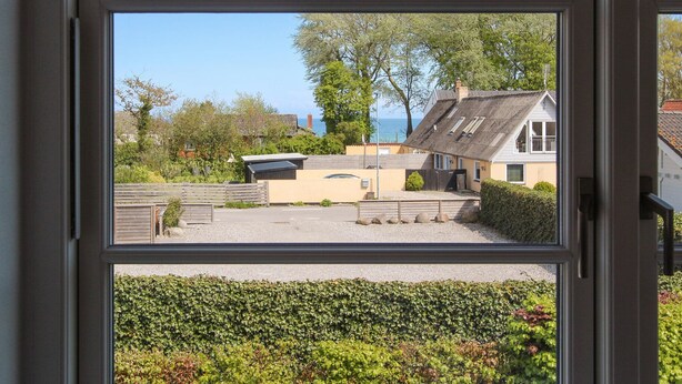 A view through a window of a residential area with a house, a small shed, and a hedge. - 3 bedroom gorgeous apartment in Samsø (Samsø)