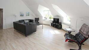 A modern loft apartment with a high ceiling, a black leather sofa, a black leather chair, a small table, a TV, and artwork on the walls. - 3 bedroom gorgeous apartment in Samsø (Samsø)