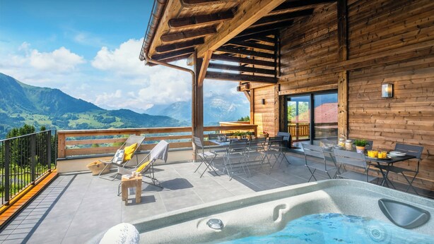 A wooden cabin with a hot tub, outdoor seating, and a mountain view.
