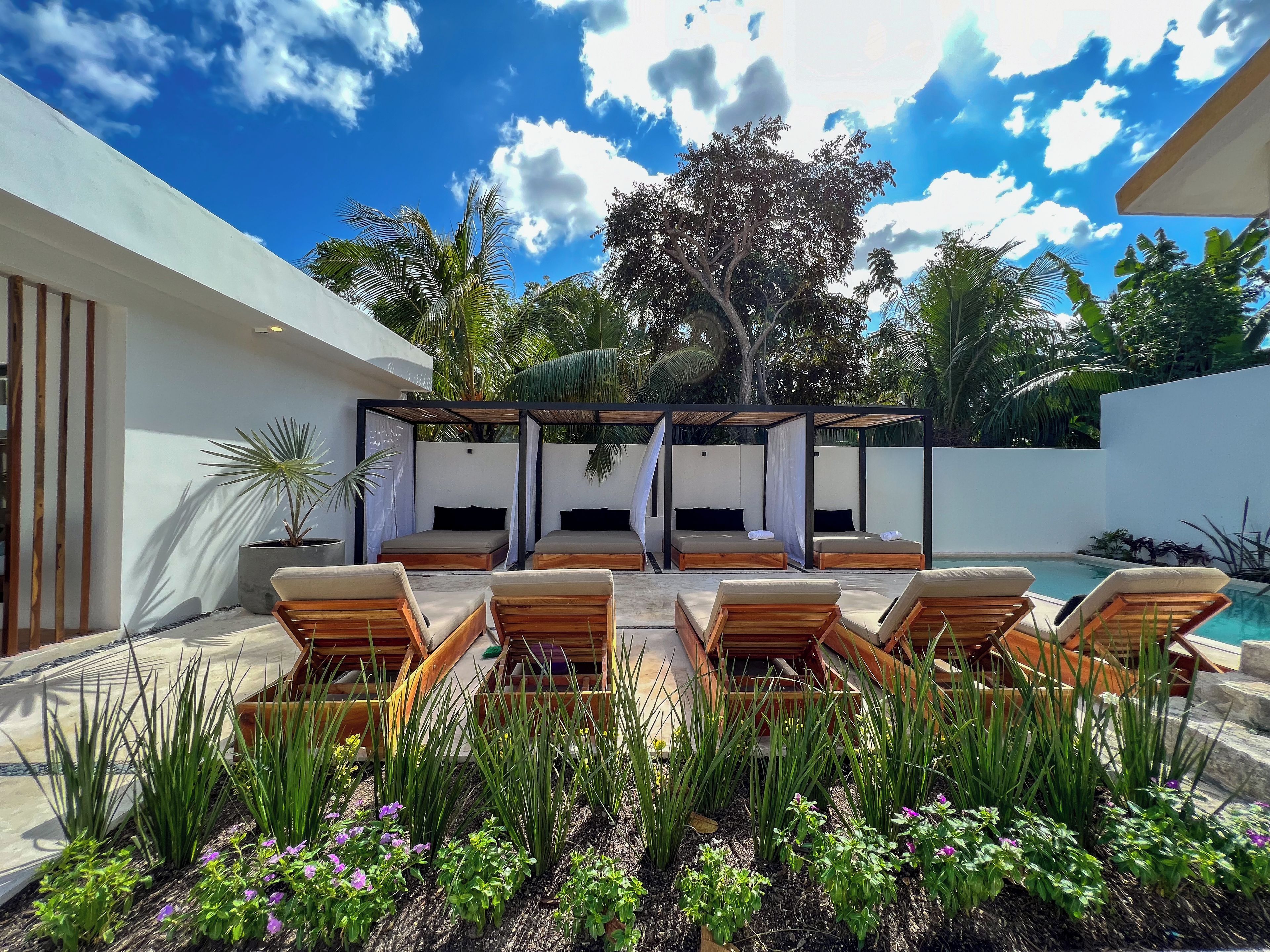 Un espacio lounge moderno al aire libre con tumbonas de madera, una zona de estar cubierta y una piscina.