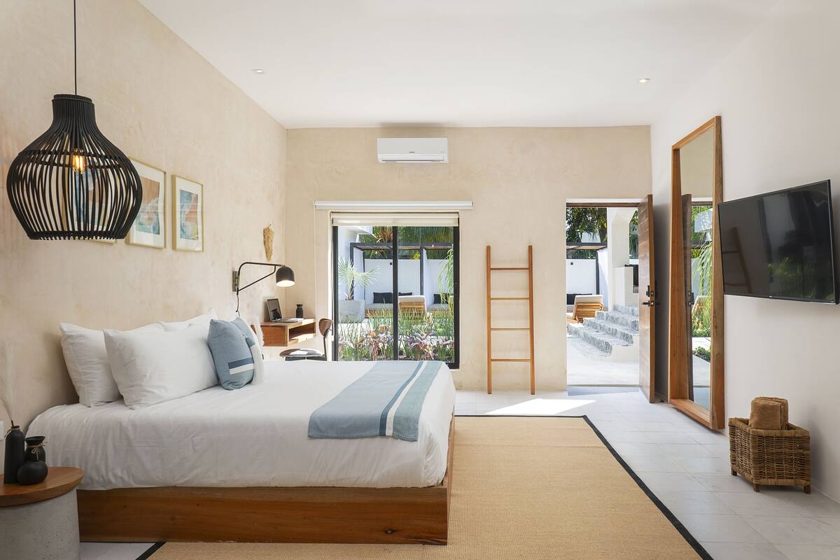 A modern bedroom with a large bed, a TV, and a view of the outdoors.
