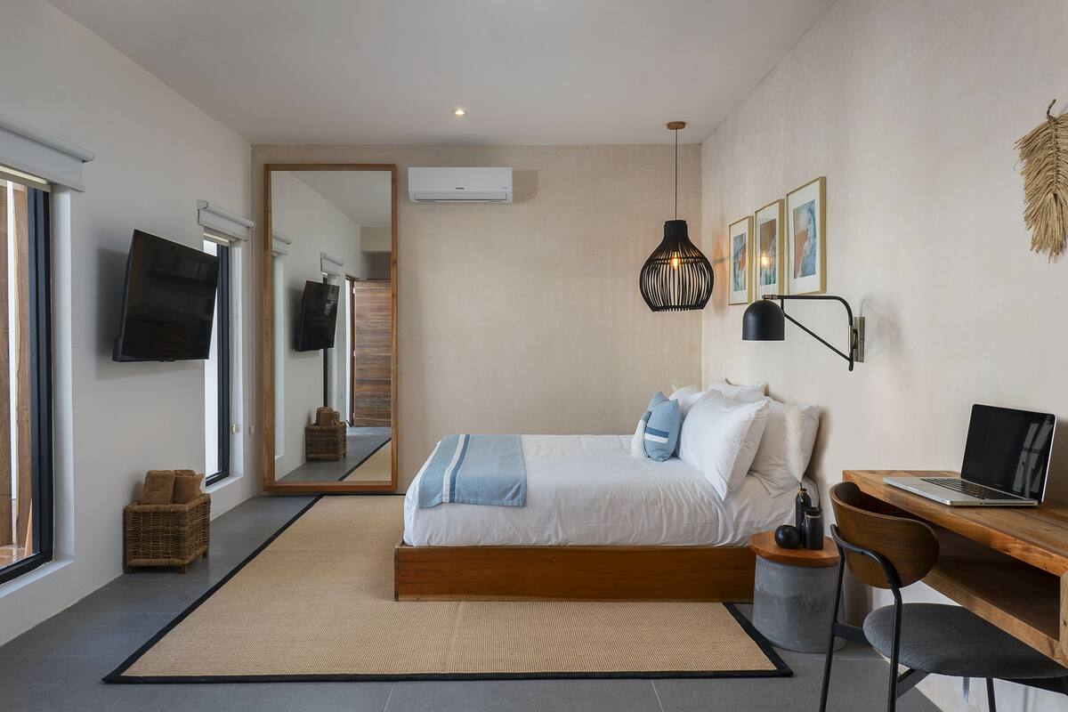 A modern bedroom with a bed, a desk, a laptop, and a TV.