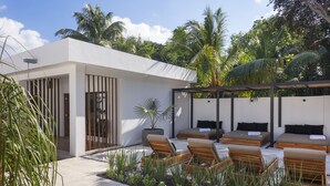 A modern outdoor lounge area with wooden loungers and a covered seating area, surrounded by lush greenery and palm trees. - Illa Cozumel (Cozumel)