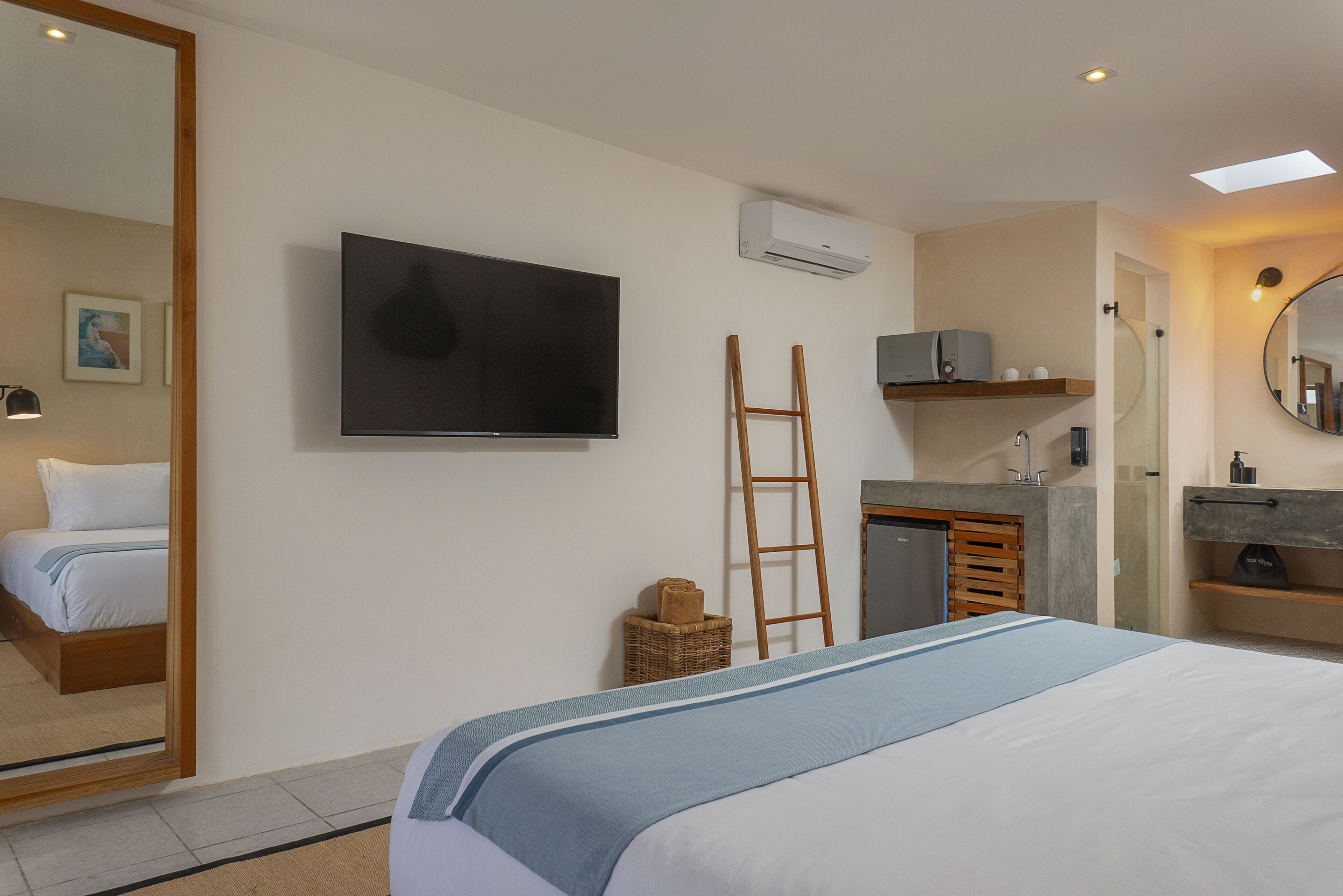 A hotel room with a bed, a television, a bathroom with a mirror, and a small shelf with toiletries.