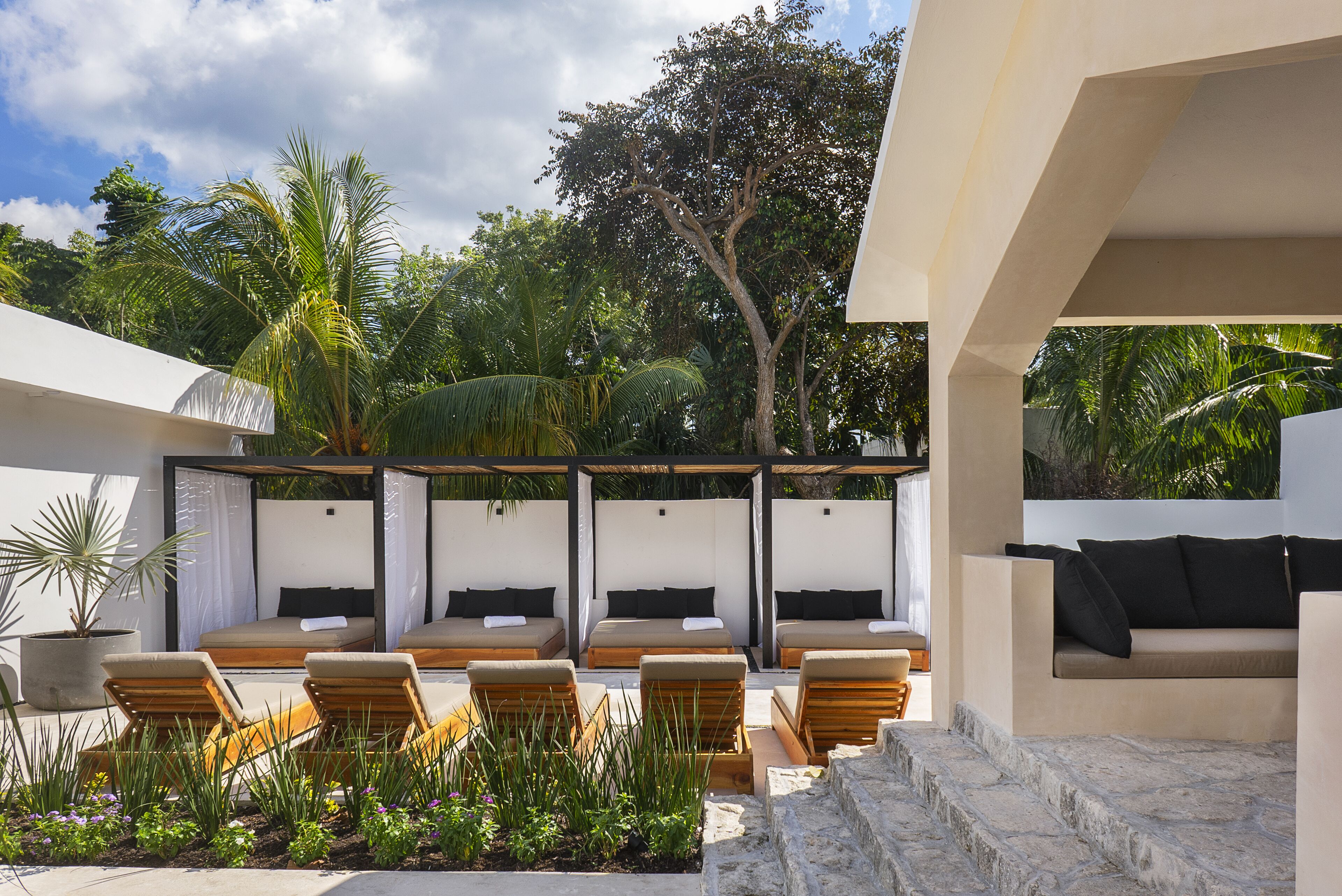 Un área de descanso exterior moderna con varias opciones de asiento, incluyendo sillones y un sofá, rodeada de exuberante vegetación y un sendero de piedra.