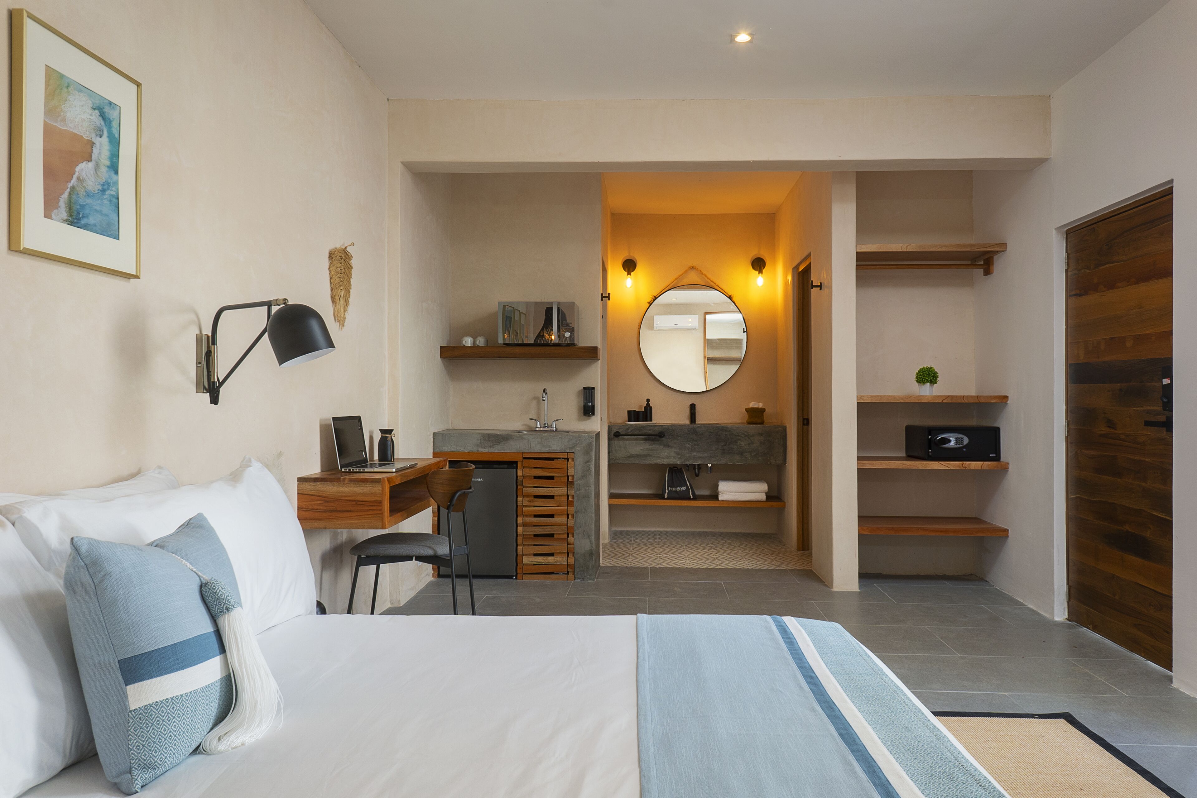 A modern hotel room with a bed, desk, and a small kitchenette.