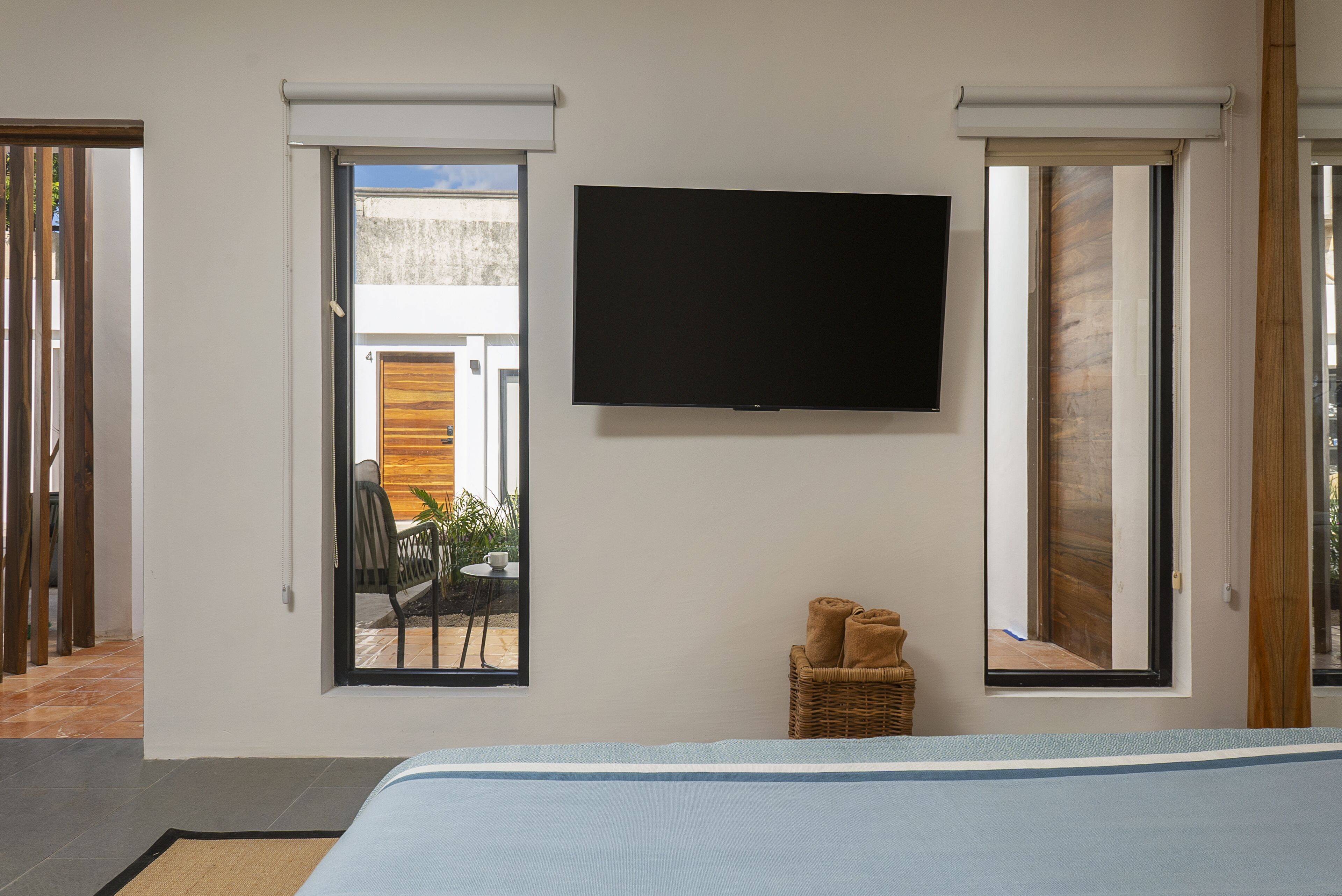 Un dormitorio con una cama, un televisor de pantalla plana montado en la pared, una silla de mimbre y una mesita con una toalla.