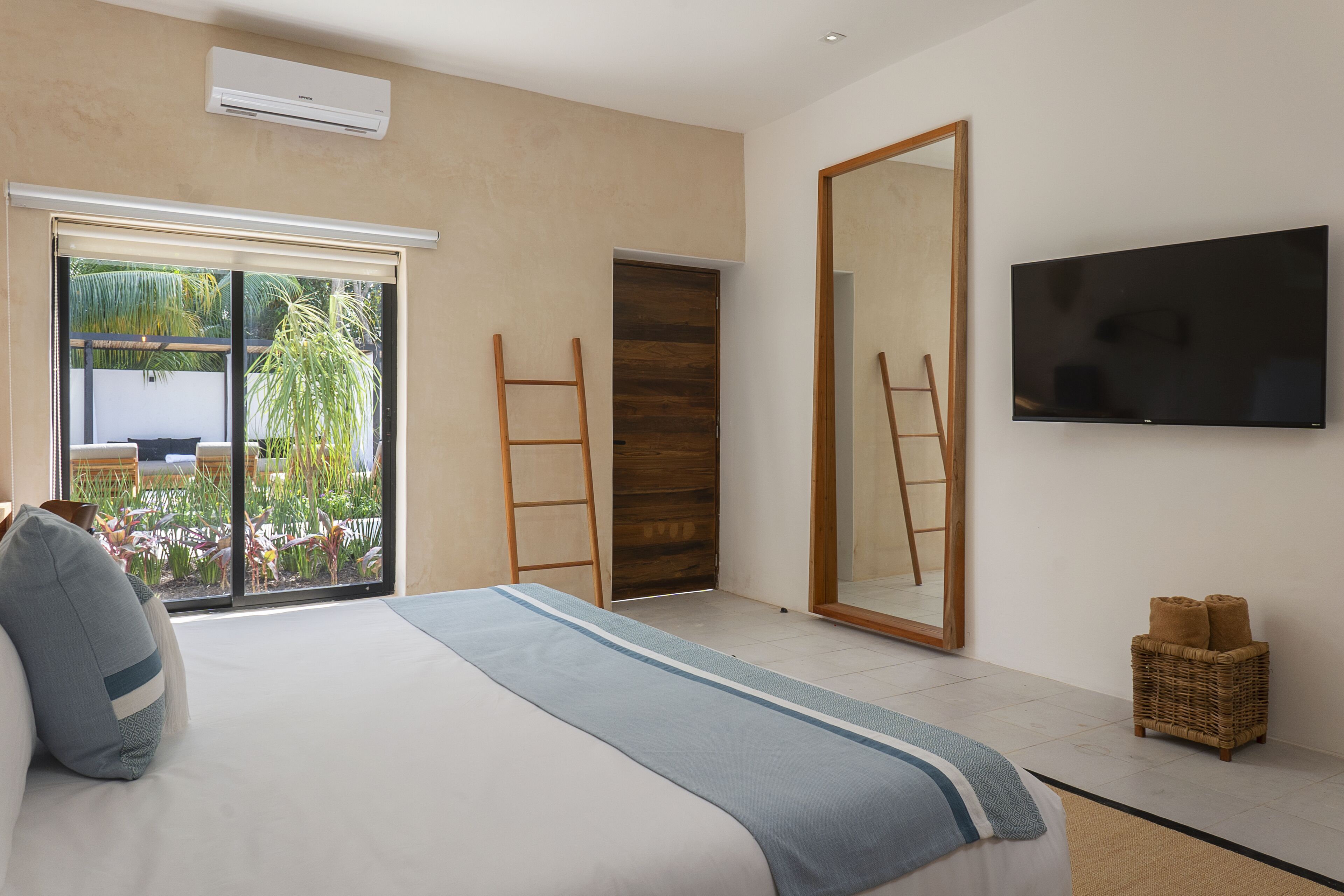 A bedroom with a bed, a TV, a large mirror, and a view of a garden through a sliding door.