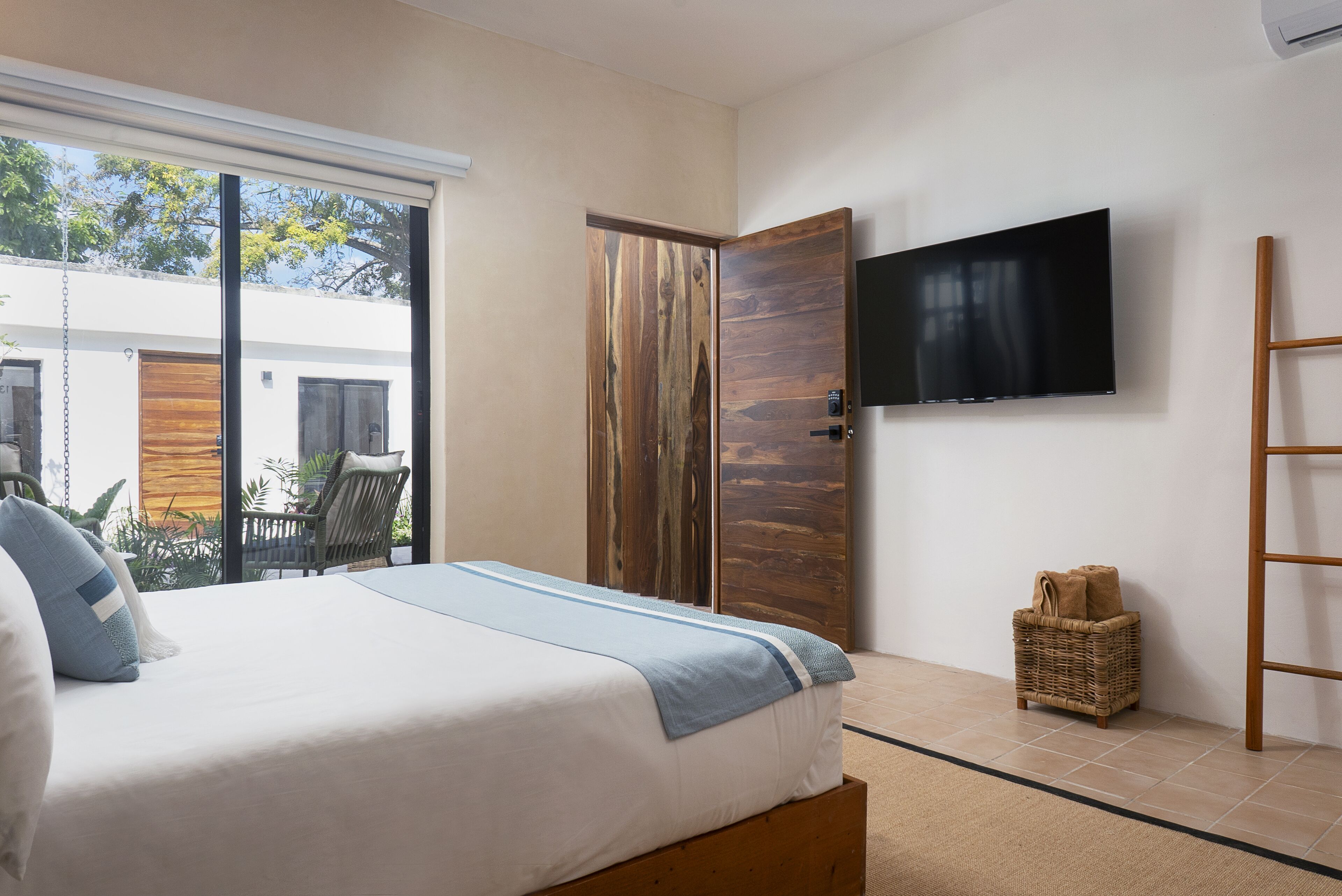 Une chambre à coucher avec un lit, un téléviseur fixé au mur, un panier en osier et une échelle en bois.