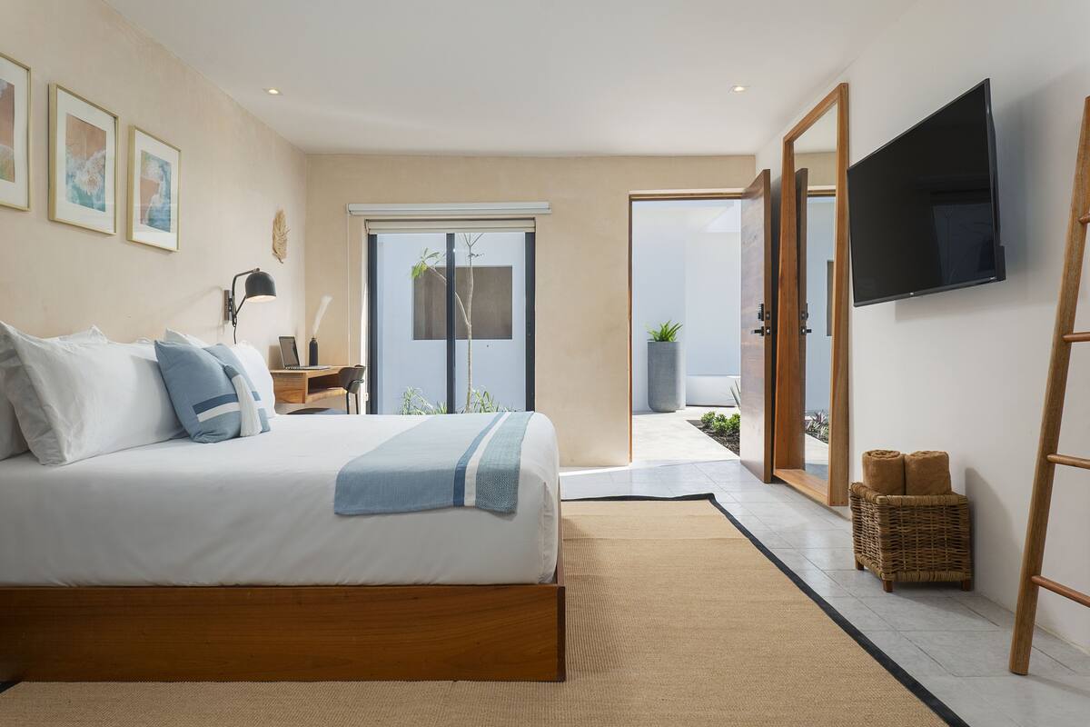 A modern bedroom with a large bed, a flat-screen TV, and a sliding glass door leading to a balcony.