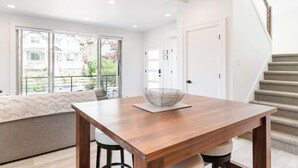 A modern dining area with a wooden table, a woven basket, and a view of a balcony with a sofa. - Spotless Modern Steps from the Best Shops and Restaurants. (Portland)