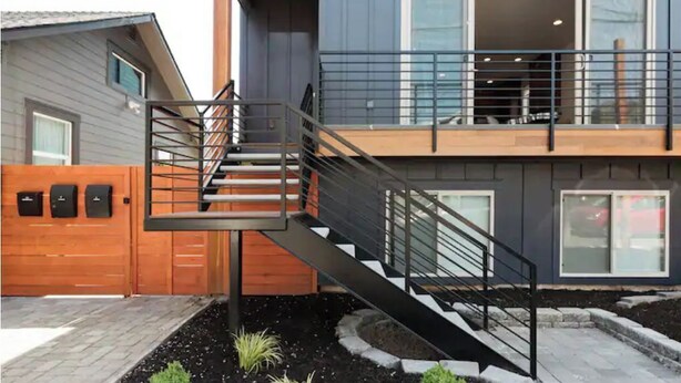 A modern two-story house with a wooden deck, a staircase with metal railings, and a garage door. - Spotless Modern Steps from the Best Shops and Restaurants. (Portland)