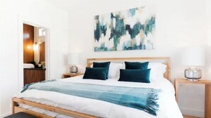 A neatly made bed with a blue and white bedspread, two bedside lamps, and a modern abstract painting on the wall. - Spotless Modern Steps from the Best Shops and Restaurants. (Portland)