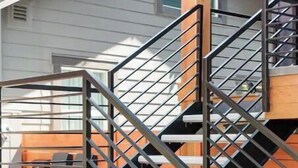 A modern outdoor staircase with metal railings and wooden steps, leading to a covered area with outdoor furniture. - Spotless Modern Steps from the Best Shops and Restaurants. (Portland)
