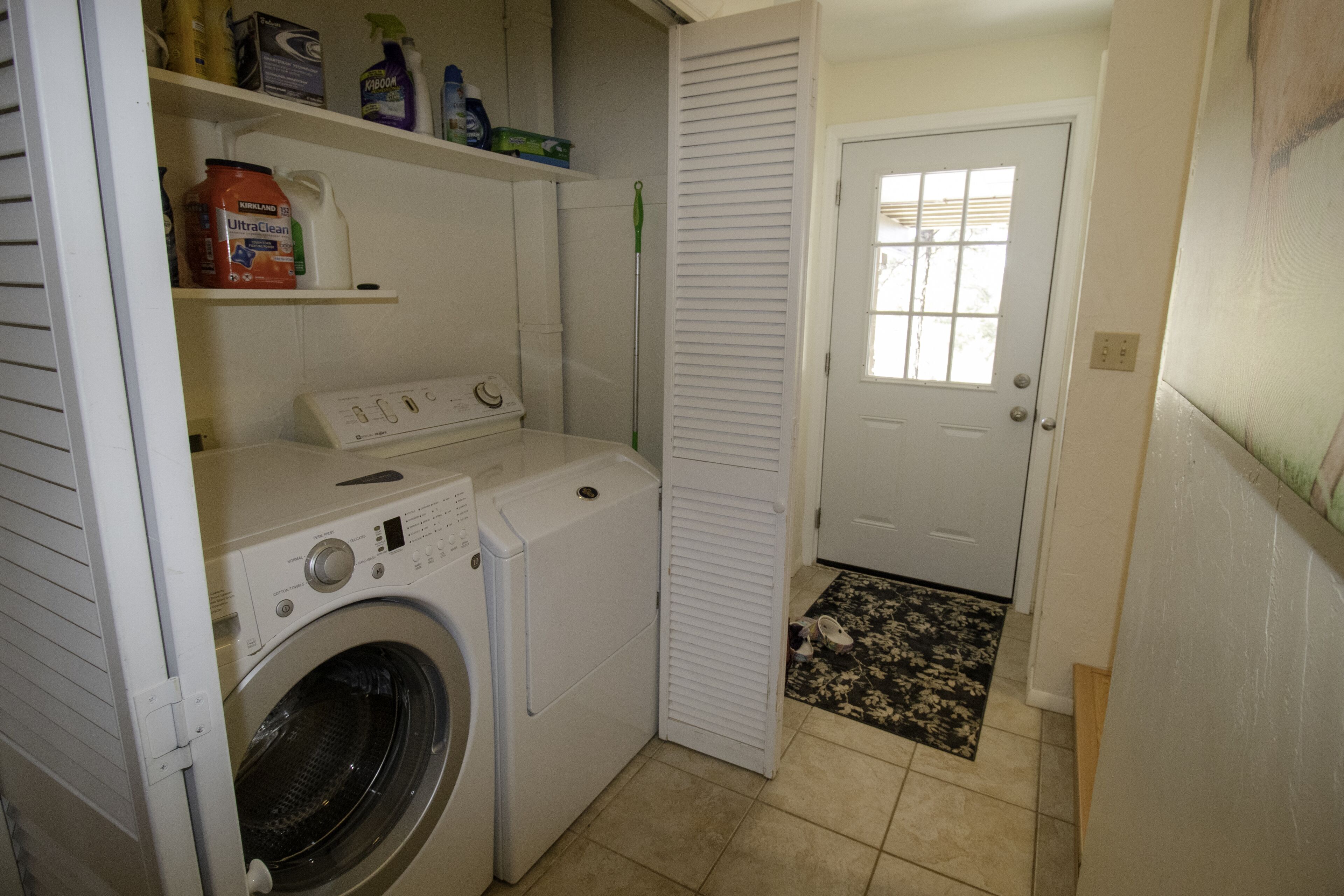 Un espace buanderie comprenant un lave-linge, un sèche-linge et des étagères où sont rangés les produits de nettoyage.
