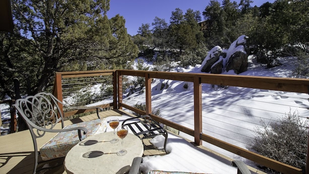 A wooden deck with a table and chairs, overlooking a snowy landscape with trees and rocks.