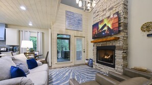 A living room with a stone fireplace, a sofa, and a television. - Pet-Friendly Cabin 5 minutes from town with stunning decor and views! (Broken Bow)