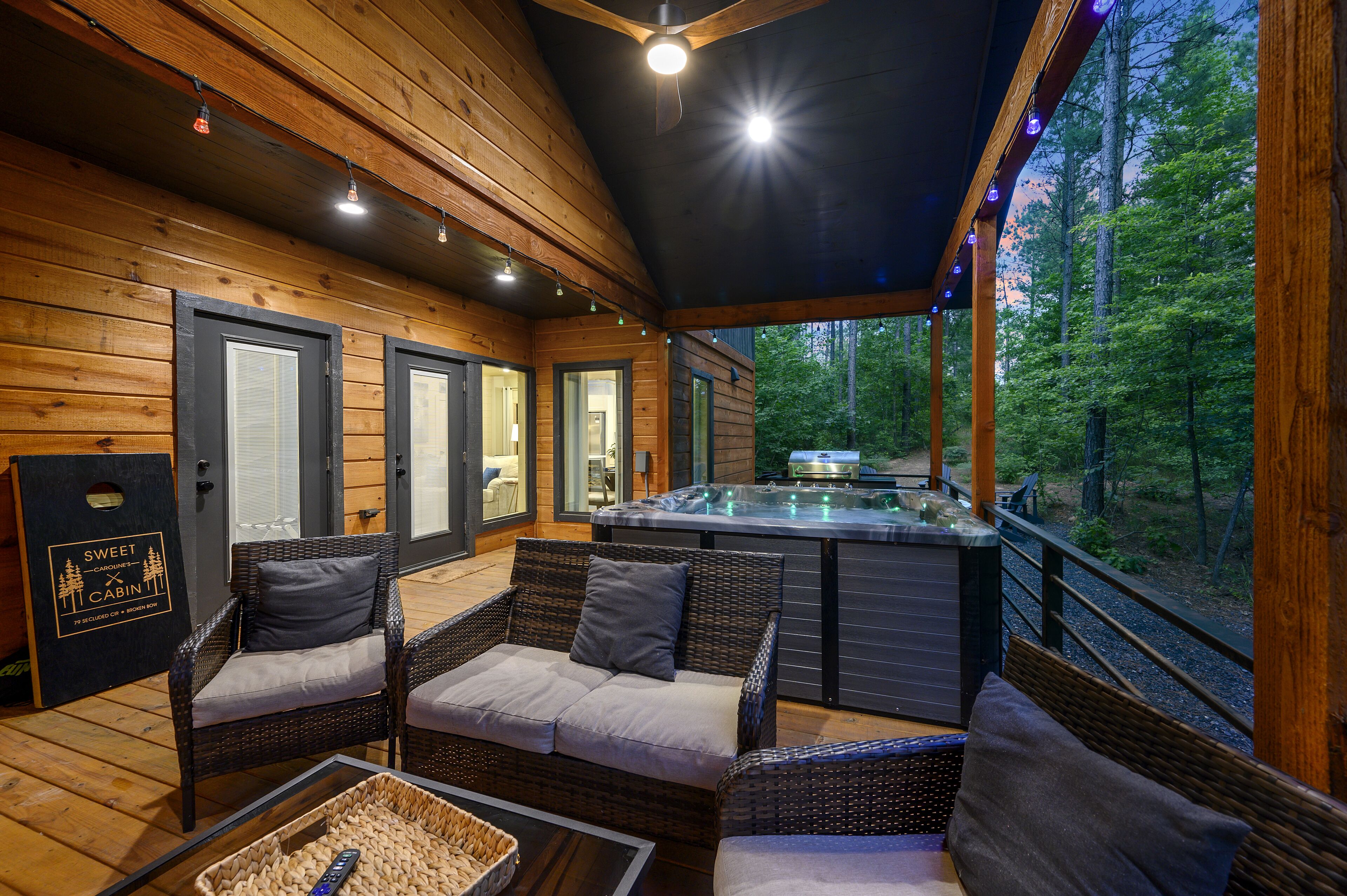 A cabin with wicker furniture, a hot tub, and a view of the forest.