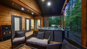 A cabin with wicker furniture, a hot tub, and a view of the forest.
