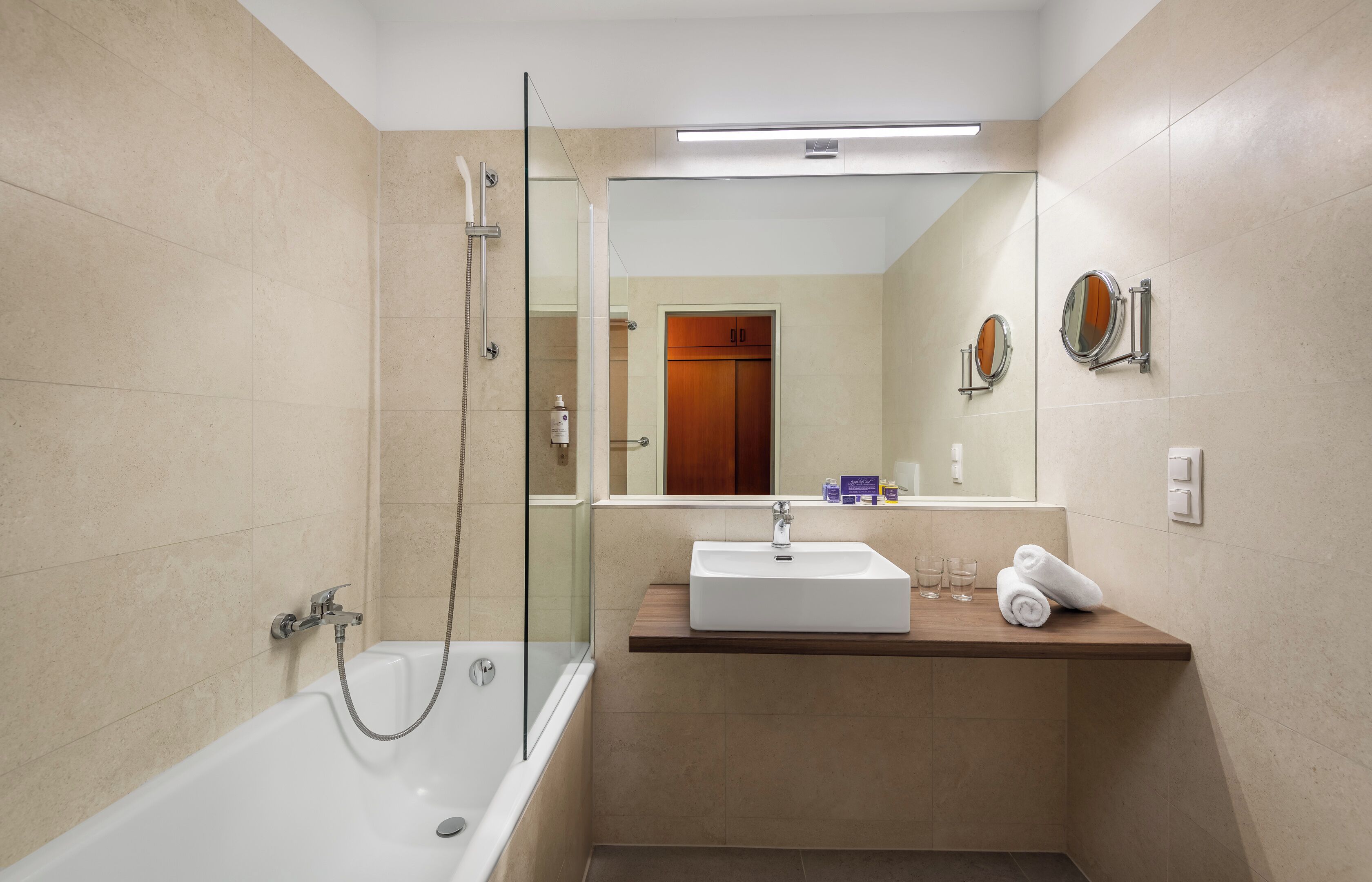 A modern bathroom with a glass-enclosed shower, a white sink, and a wooden vanity.