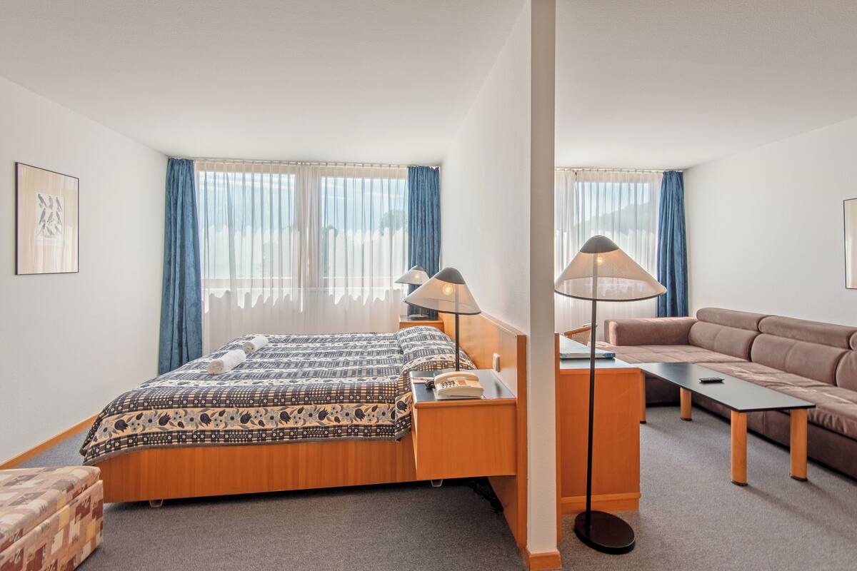 A hotel room with a bed, a sofa, a desk, and a lamp.