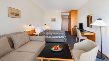Habitación de hotel con cama, sofá, escritorio, silla, una mesita con fruta y lámpara.