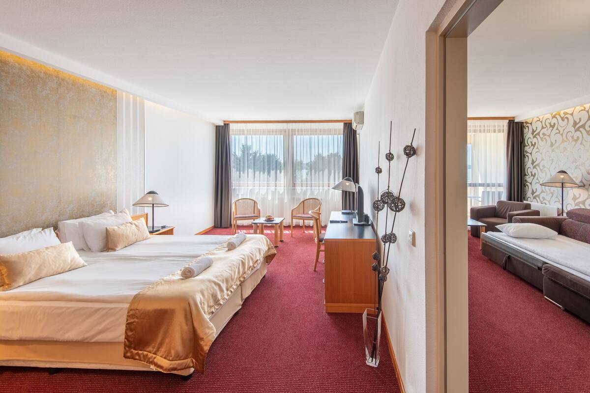 A hotel room with two beds, a desk, chairs, and a sofa.