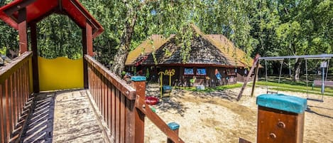 Un’area giochi con una struttura in legno, altalene e un piccolo edificio con tetto di paglia.