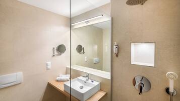 A modern bathroom with a large mirror, a sink, a showerhead, and a towel rack.
