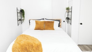 Een keurig opgeruimde slaapkamer met een bed, een zacht vloerkleed en twee wandplanken met planten.