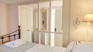 A bedroom with a bed, a nightstand, a lamp, a heart-shaped decoration, and a wardrobe with a mirror. - The Old Barn (Colyton)