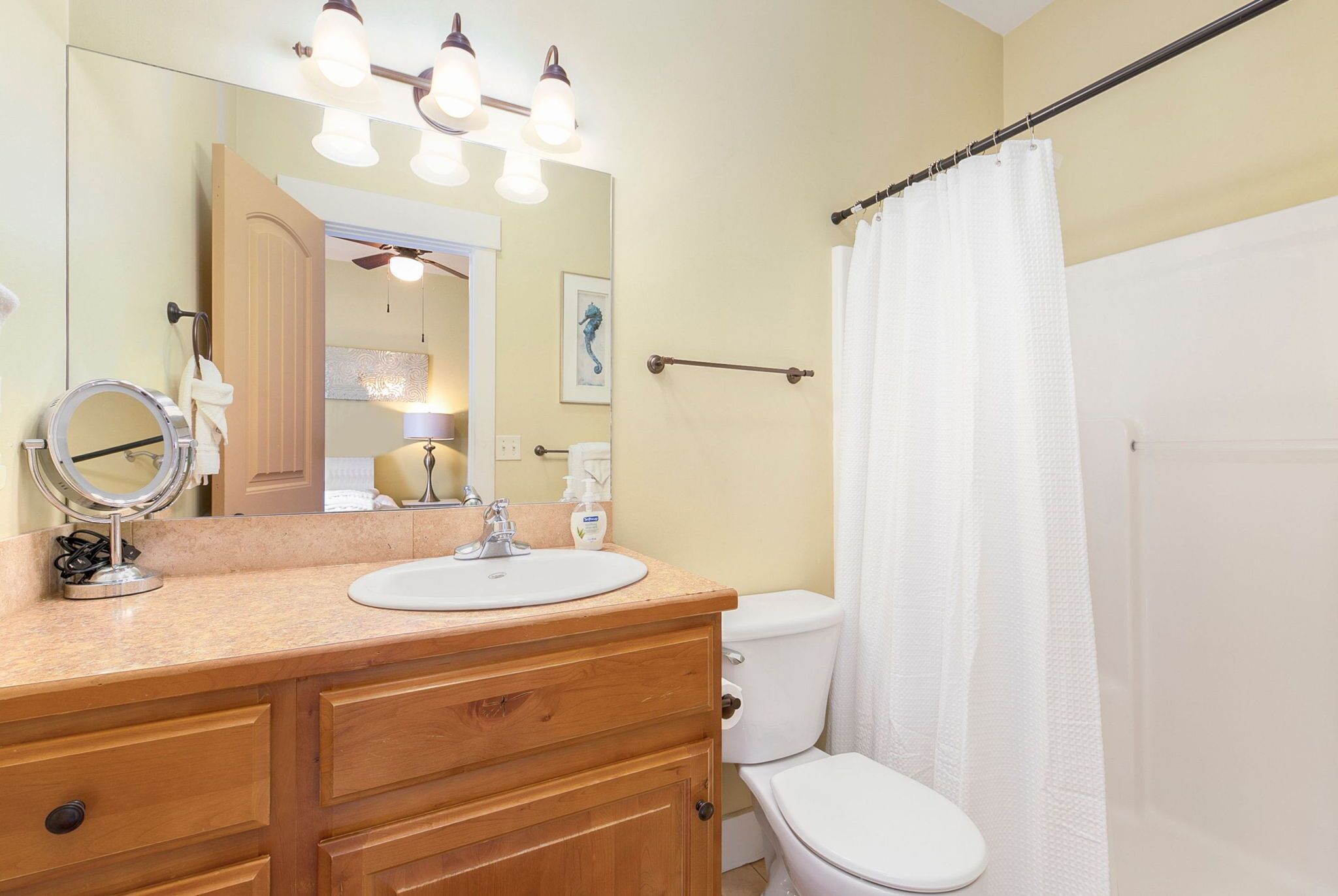 A bathroom with a wooden vanity, a round mirror, a white sink, and a white toilet.