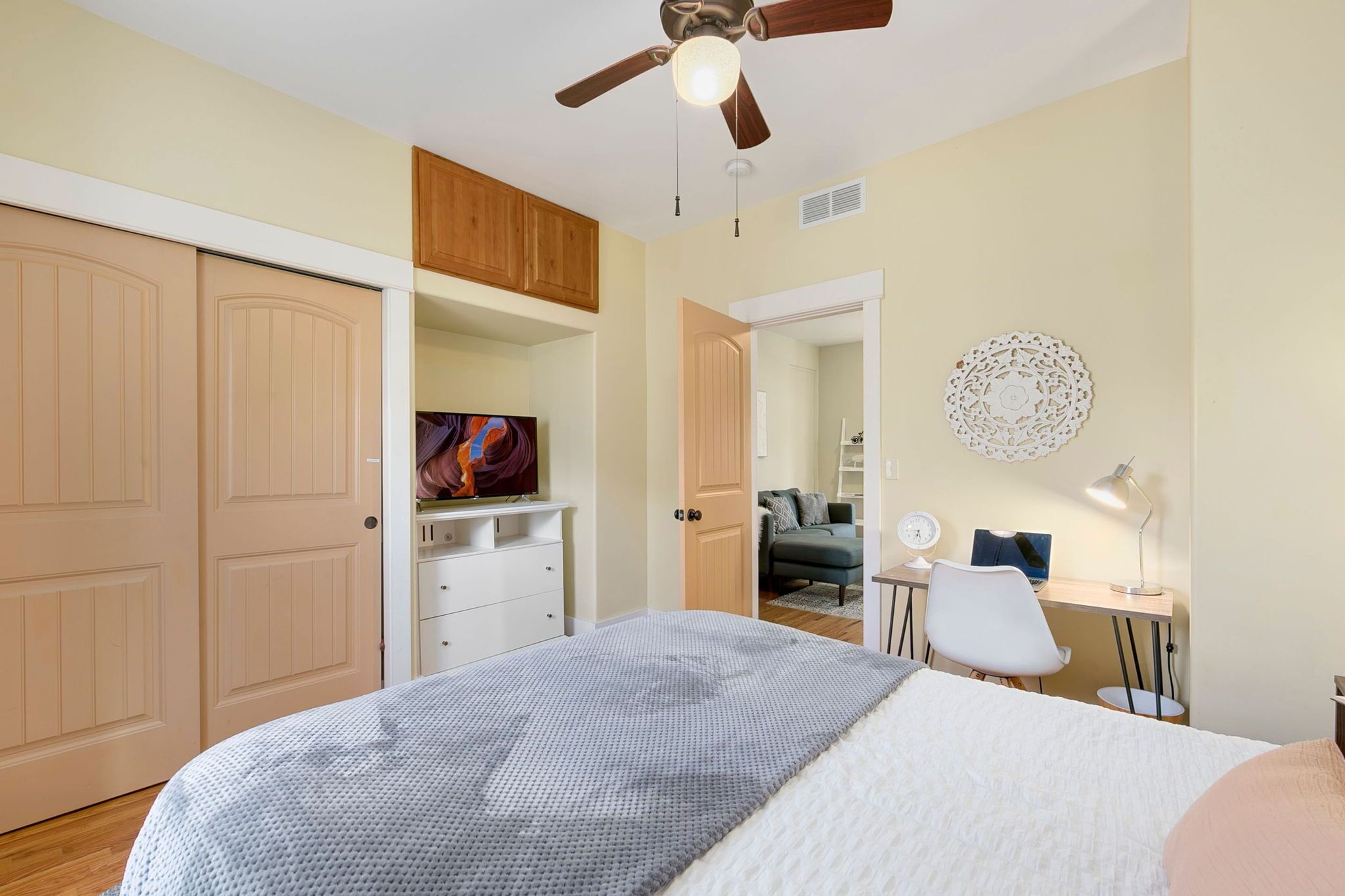 Une chambre à coucher comprenant un lit, un ventilateur de plafond, un bureau avec une chaise, une télévision et une armoire.