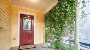 A red door with a glass panel, a welcome mat, and a porch with a green vine. - Walk Everywhere - Art, Restaurants, Poudre River (Fort Collins)
