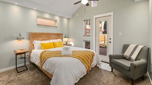A bedroom with a bed, a bedside table, a chair, a ceiling fan, and a door leading to a balcony. - Vibrant Downtown Bungalow – Walk Everywhere! (Fort Collins)