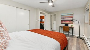 Une chambre à coucher avec un lit, un bureau, une chaise, un ventilateur de plafond et un tableau accroché au mur.