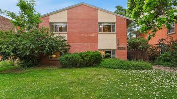 A two-story brick building with a flat roof, surrounded by a well-maintained lawn and flowering plants.