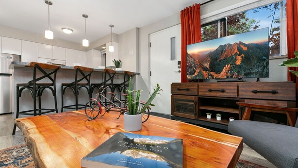 Un salon moderne avec une table basse en bois, un livre intitulé « Colorado : un atlas historique » et un grand téléviseur à écran plat qui diffuse un paysage de montagne.