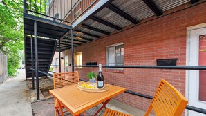 Une terrasse extérieure avec un mur en briques, un escalier en métal et une table avec des chaises.