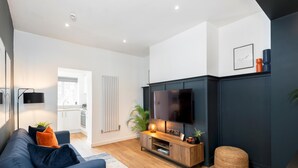 Un salon moderne avec un mur d’accent de couleur foncée, un téléviseur à écran plat, une table basse en bois et un canapé bleu agrémenté de coussins.