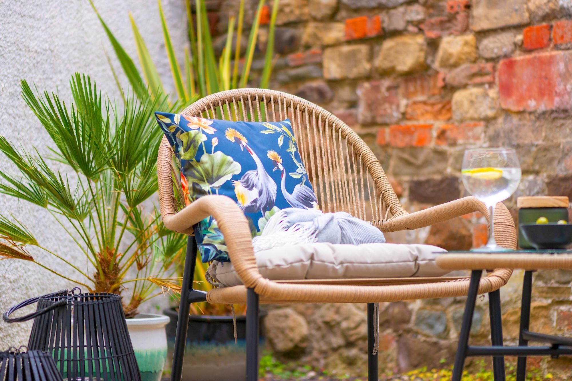 A wicker chair with a cushion and a floral pillow, placed on a table with a glass of water.