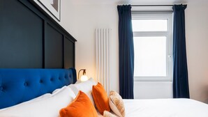 Une chambre d’hôtel avec une tête de lit bleue, du linge de lit blanc et deux fenêtres dotées de rideaux foncés.