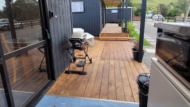 Un espacio al aire libre cubierto con una terraza de madera, una parrilla y un cochecito.